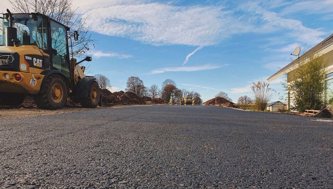 Eine Planierraupe steht am Straßenrand neben einem Haus.