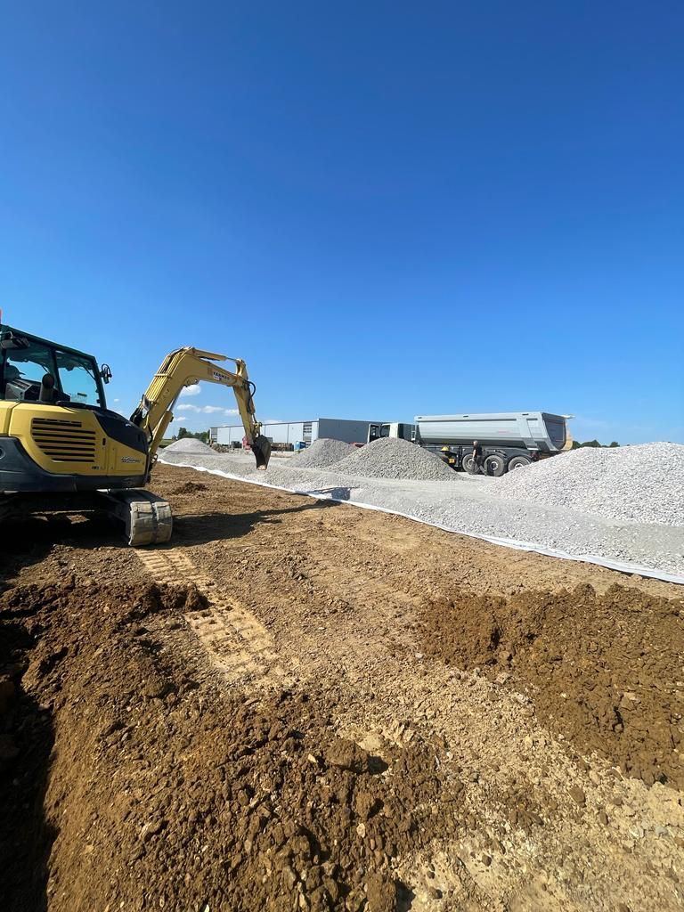 Ein gelber Bagger arbeitet auf einer unbefestigten Straße.