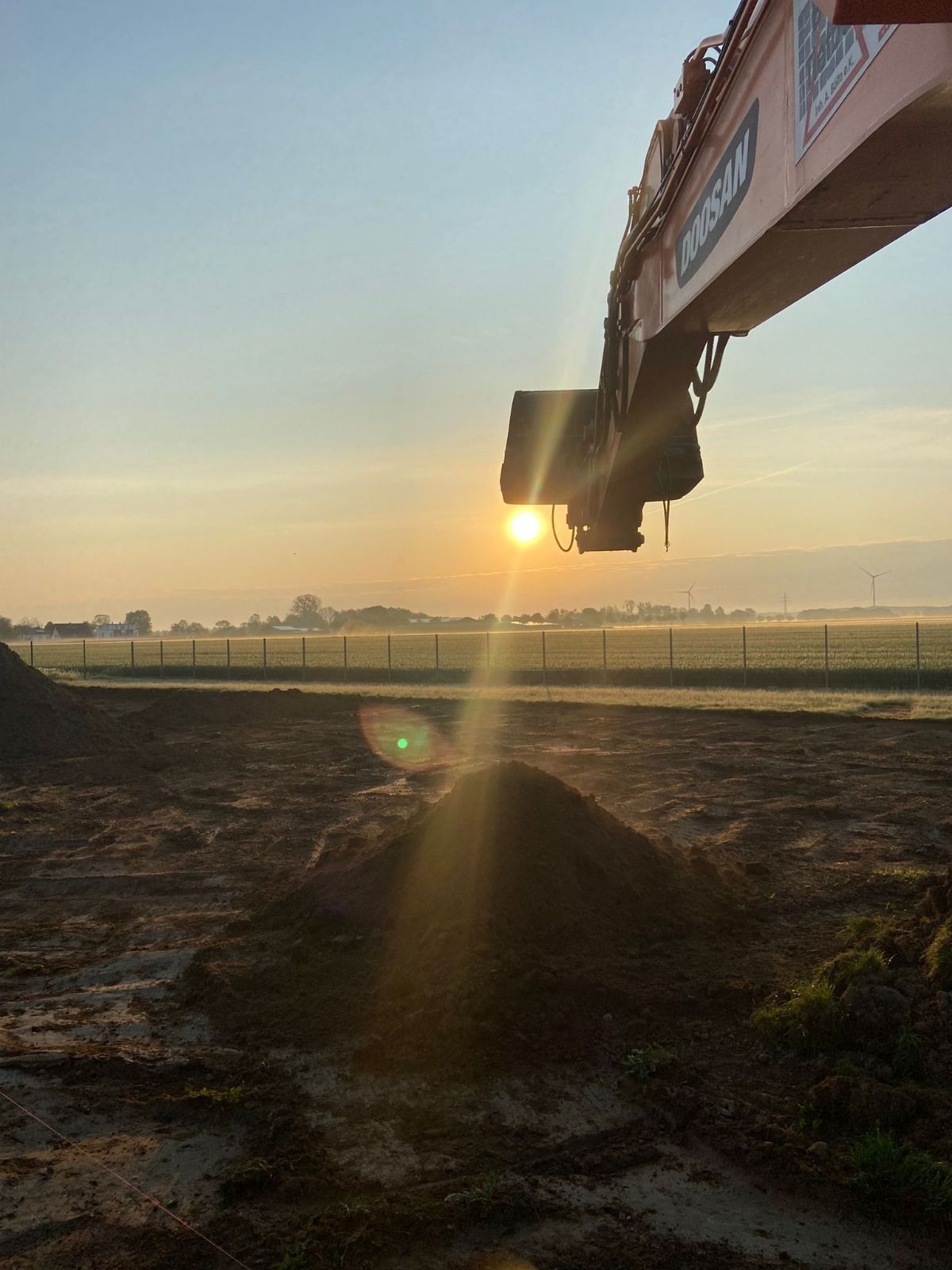 Die Sonne geht hinter einem Kran auf einem Feld unter