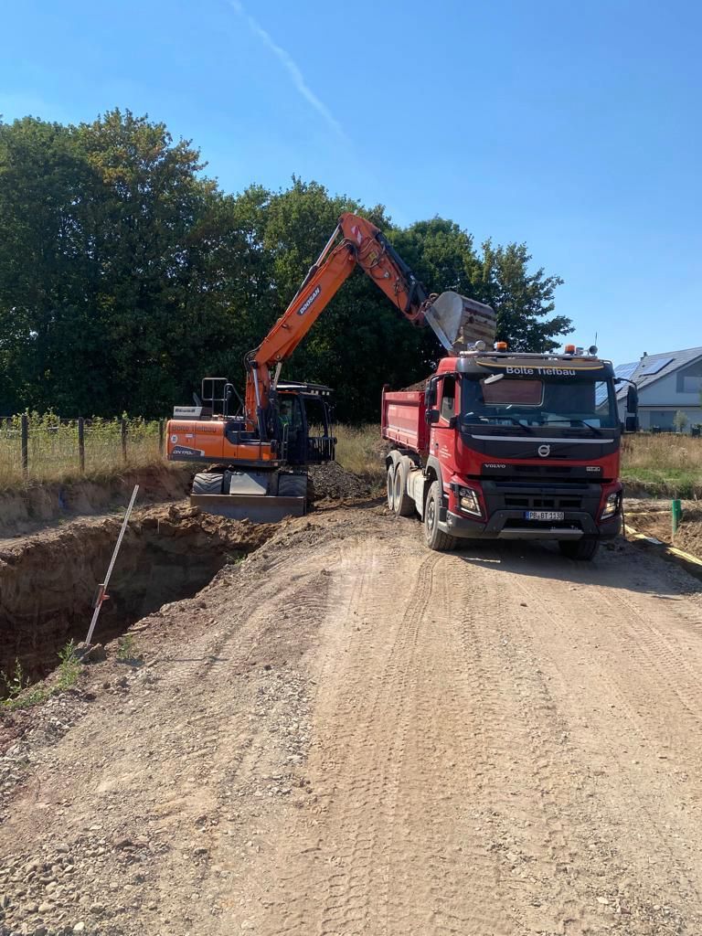 Ein Bagger lädt auf einer unbefestigten Straße Erde in einen Muldenkipper.