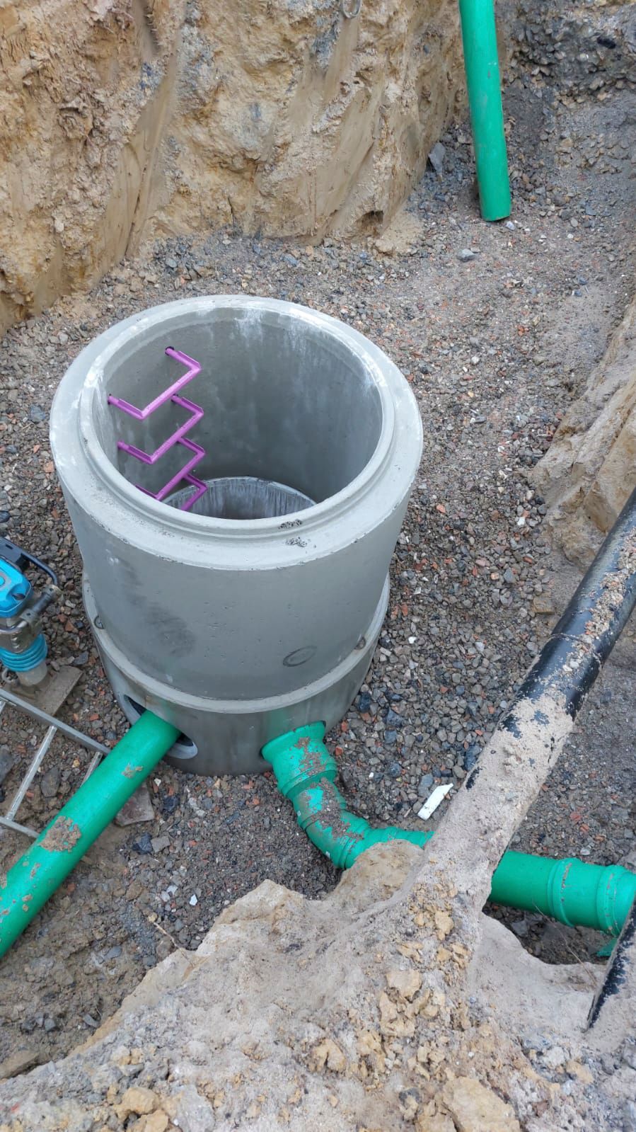 Neben grünen Rohren liegt ein Betonring im Dreck.