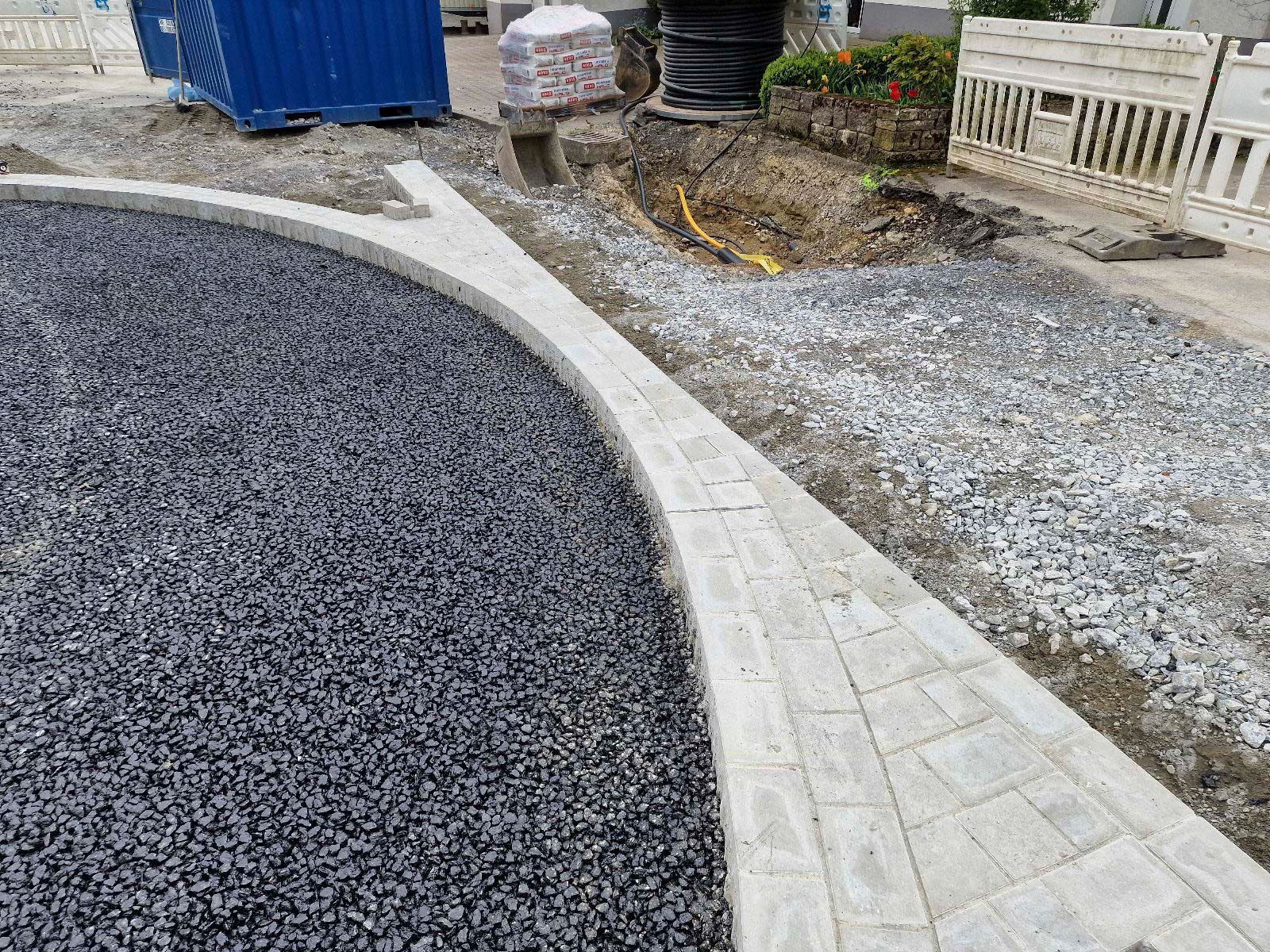 Auf einer Schotterstraße wird ein Bordstein aus Beton eingebaut.