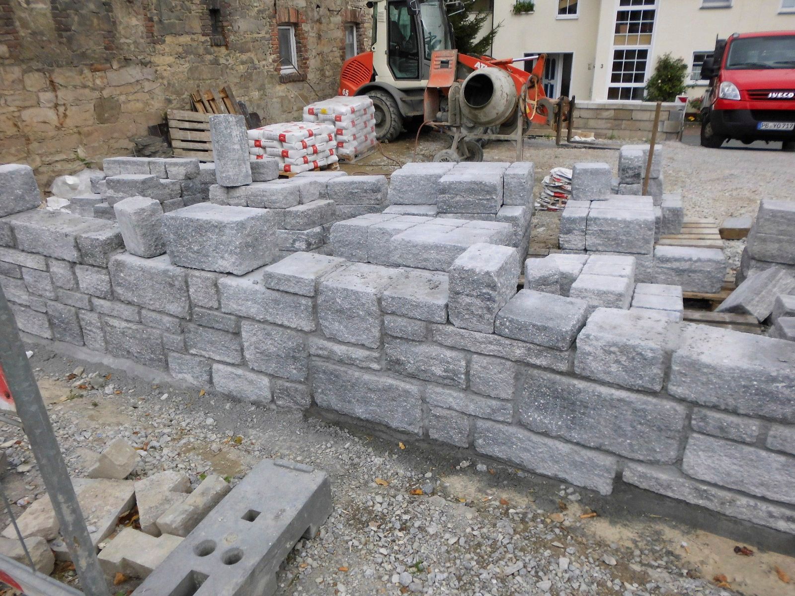 Eine Ziegelmauer wird gebaut, im Hintergrund ist ein Betonmischer zu sehen.