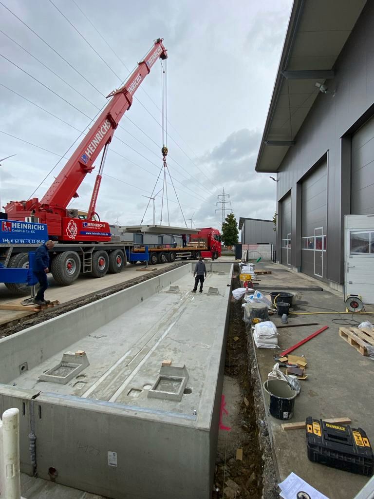 Ein roter Kran hebt einen Betonblock vor einem Gebäude an.