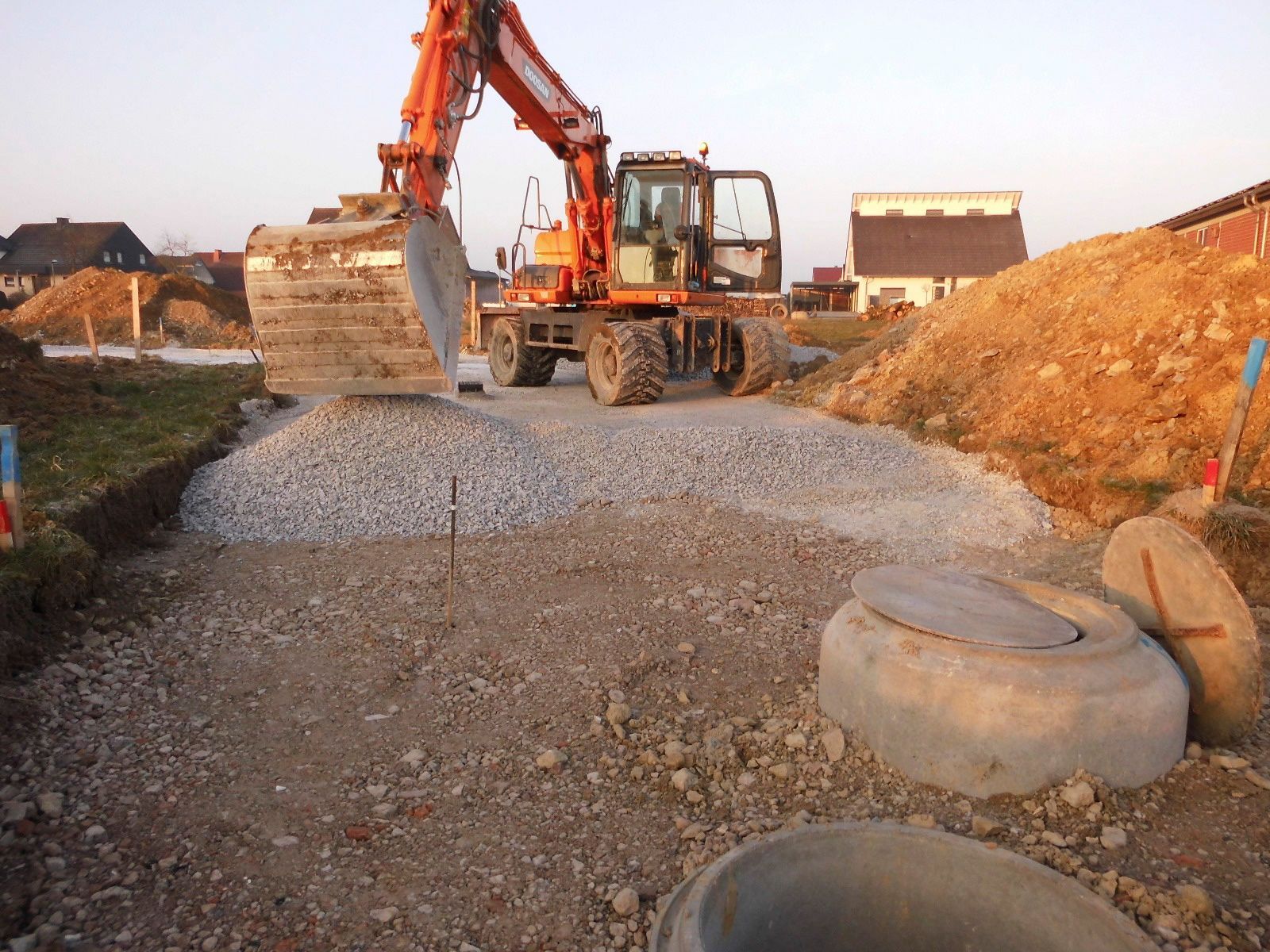 Ein großer orangefarbener Bagger bewegt Kies auf einer unbefestigten Straße