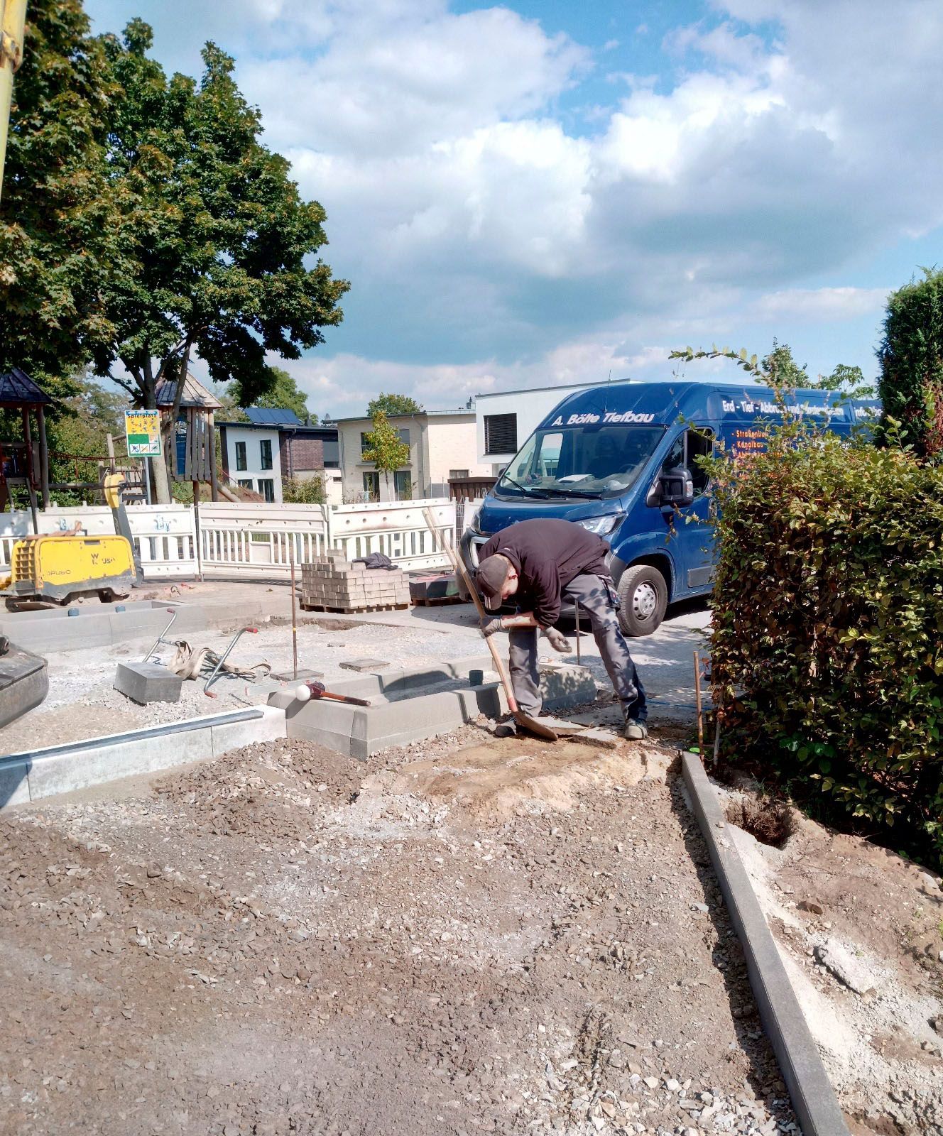 Ein Mann arbeitet auf einer Baustelle neben einem blauen Lieferwagen.