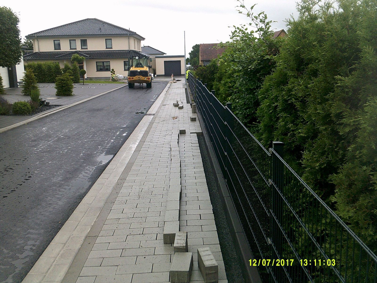 Ein gelber Lastwagen fährt eine Ziegelsteinstraße vor einem Haus entlang