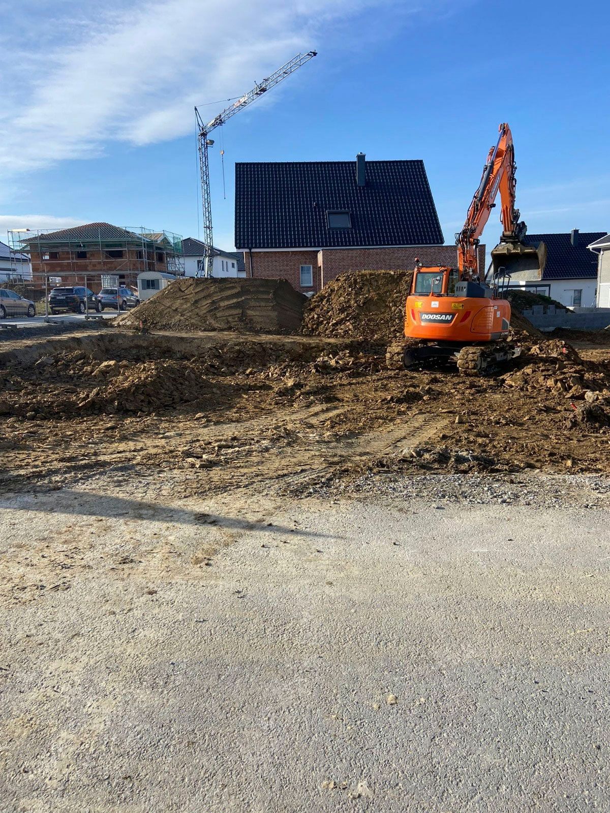 Ein großer orangefarbener Bagger arbeitet auf einer Baustelle vor einem Haus.