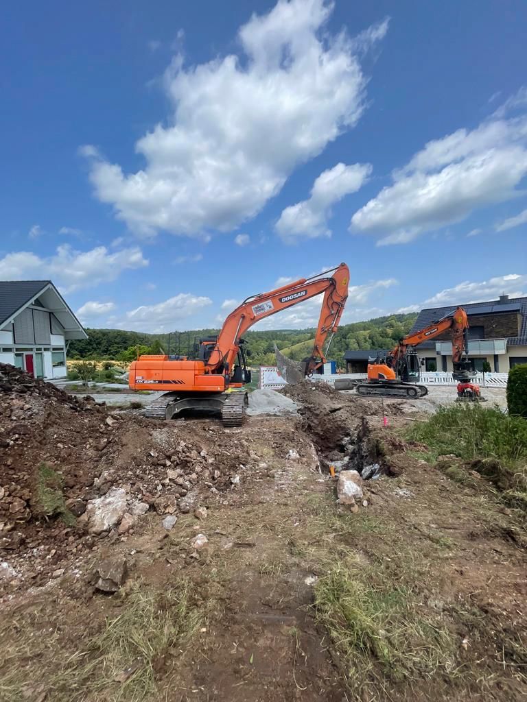 Zwei Bagger arbeiten auf einer Baustelle vor einem Haus.