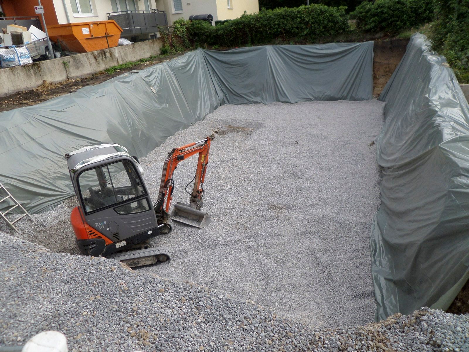 Mitten in einem Kieshaufen steht ein kleiner Bagger.
