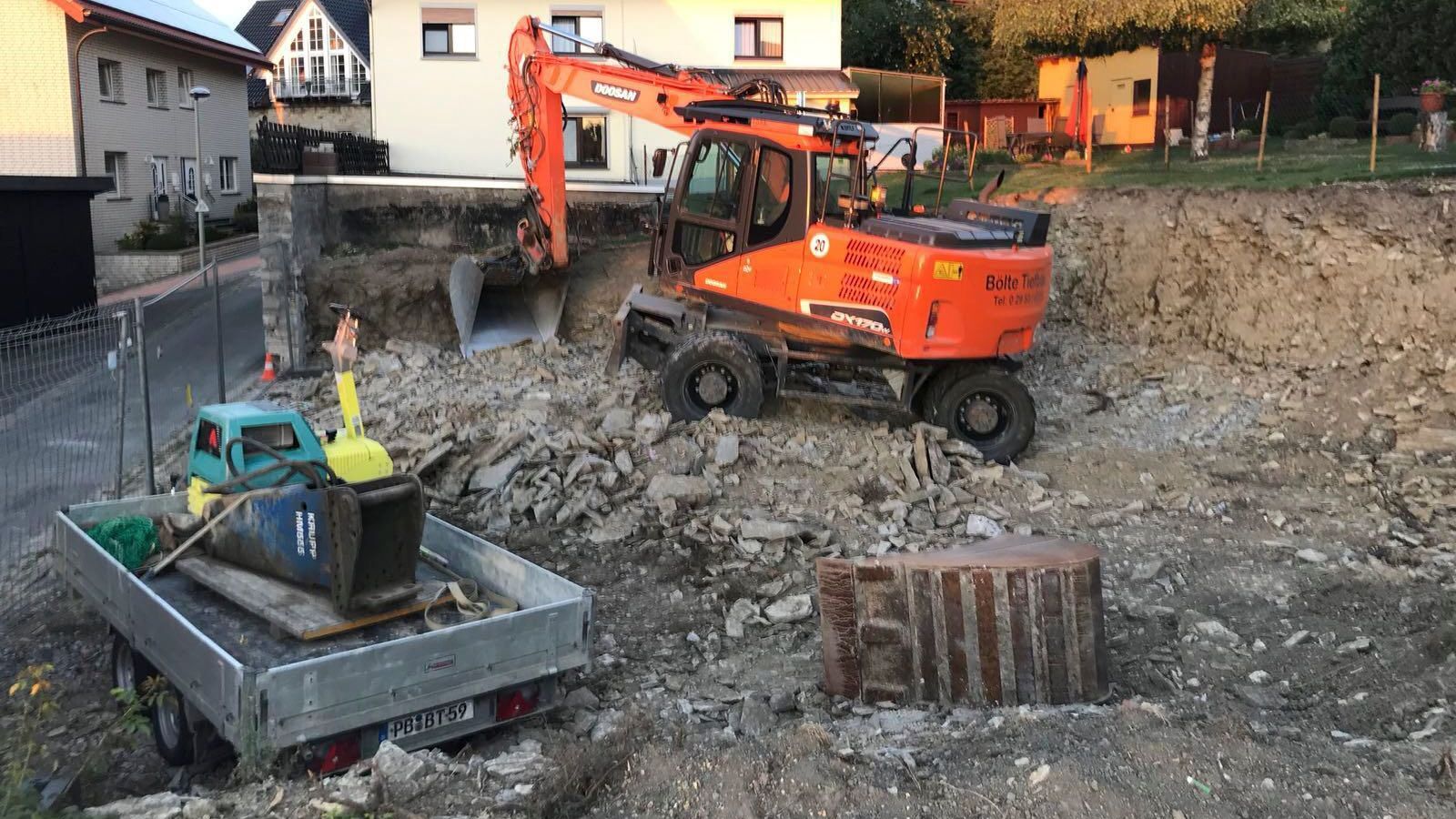 Neben einem Anhänger gräbt ein großer Bagger ein Loch in den Boden.