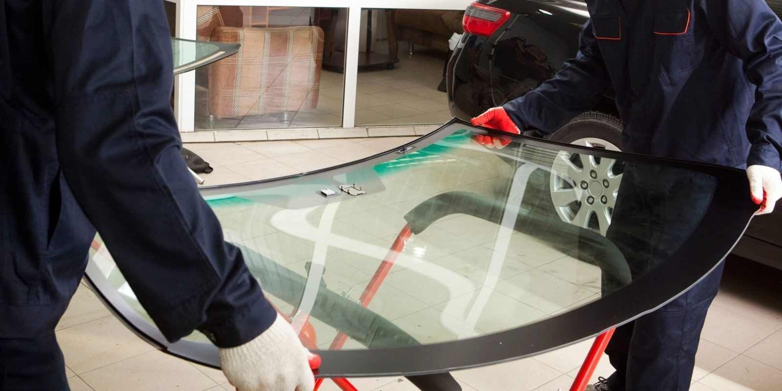 Dos hombres están instalando un parabrisas en un coche en un garaje.