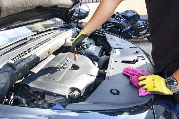 Persona con guantes amarillos comprobando el nivel de aceite del coche, compartimento del motor abierto.