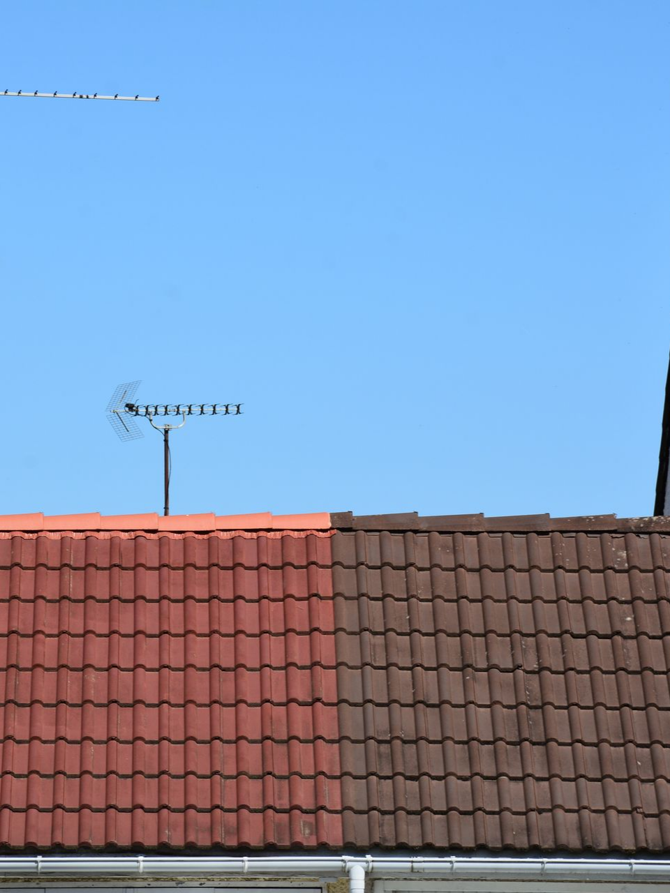 Toit de tuiles rouges et brunes avec antenne de télévision sur fond de ciel bleu.