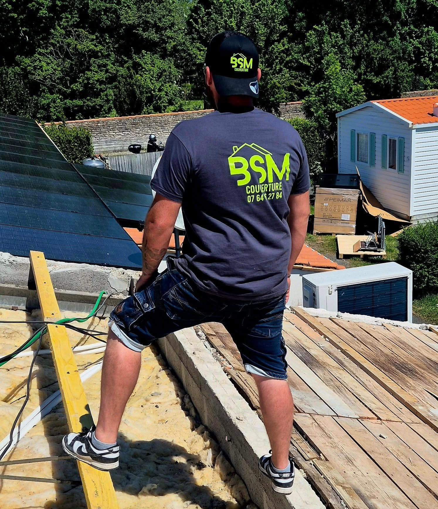 Un homme sur un toit, portant un chapeau, un t-shirt avec le logo de la société. En extérieur, il regarde ailleurs.
