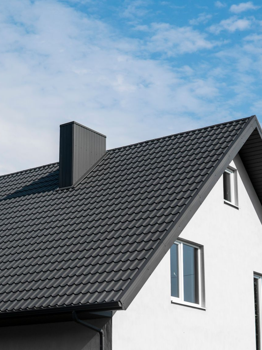 Maison blanche au toit de tuiles gris foncé et à la cheminée, se détachant sur un ciel bleu nuageux.