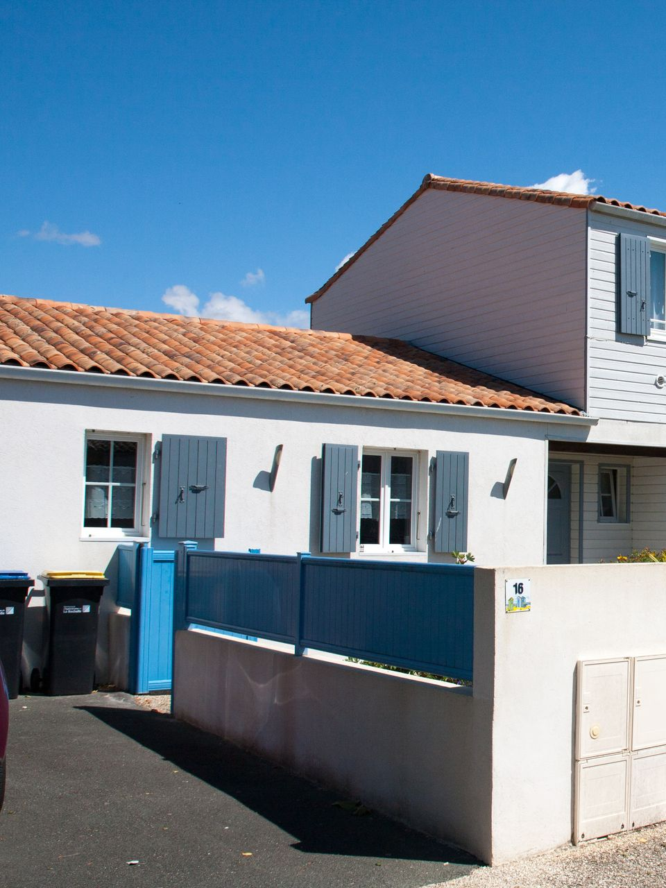 Bâtiment blanc aux volets bleus et au toit en tuiles cuites, par une journée ensoleillée.