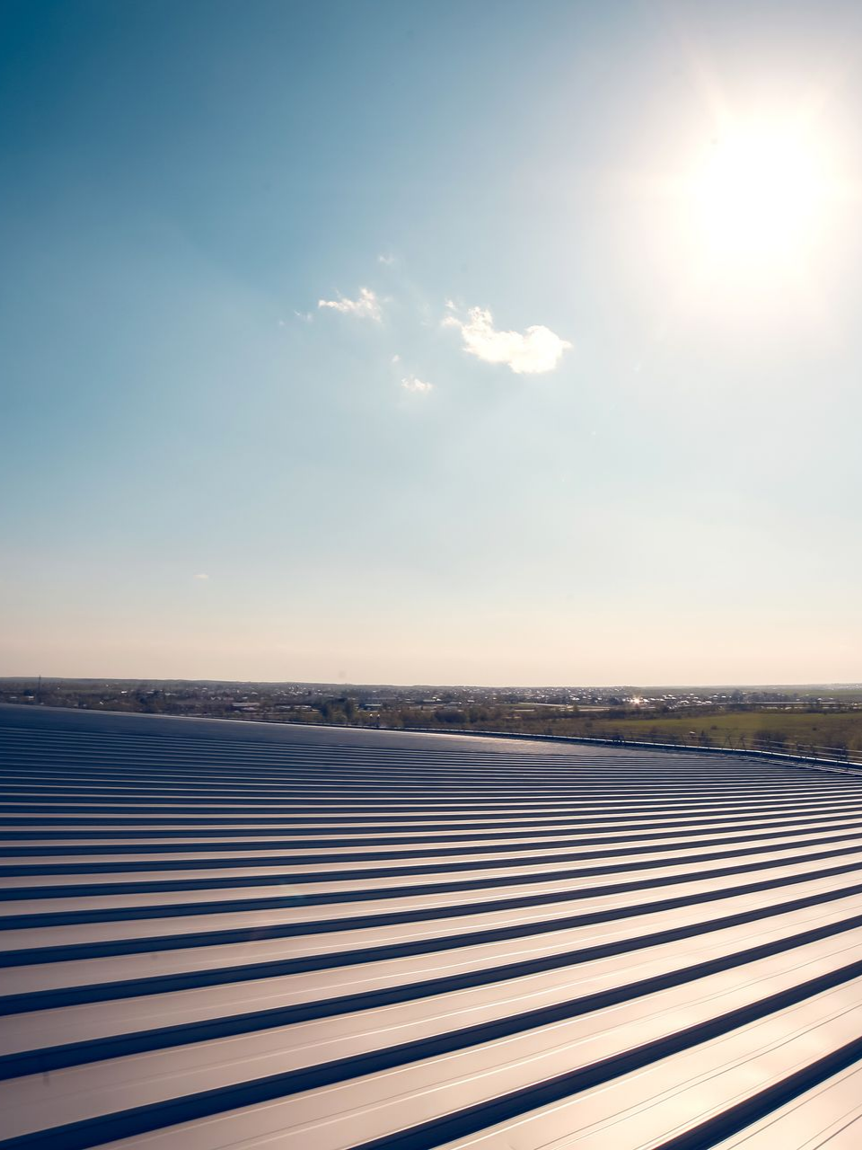 Soleil éclatant au-dessus d'un toit métallique nervuré, avec un horizon lointain sous un ciel bleu limpide.