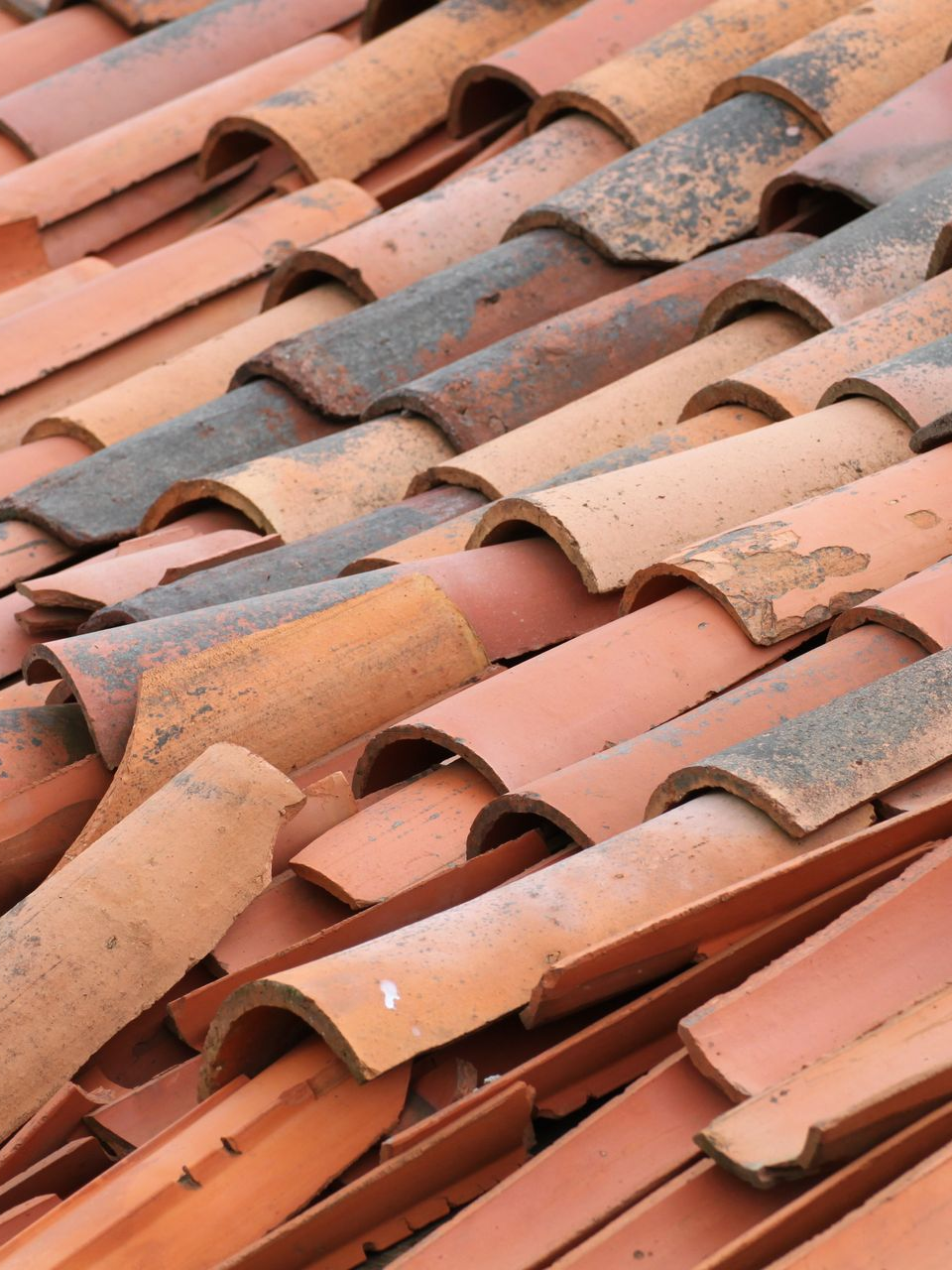 Gros plan sur des tuiles de toit incurvées en terre cuite rouge et grise.