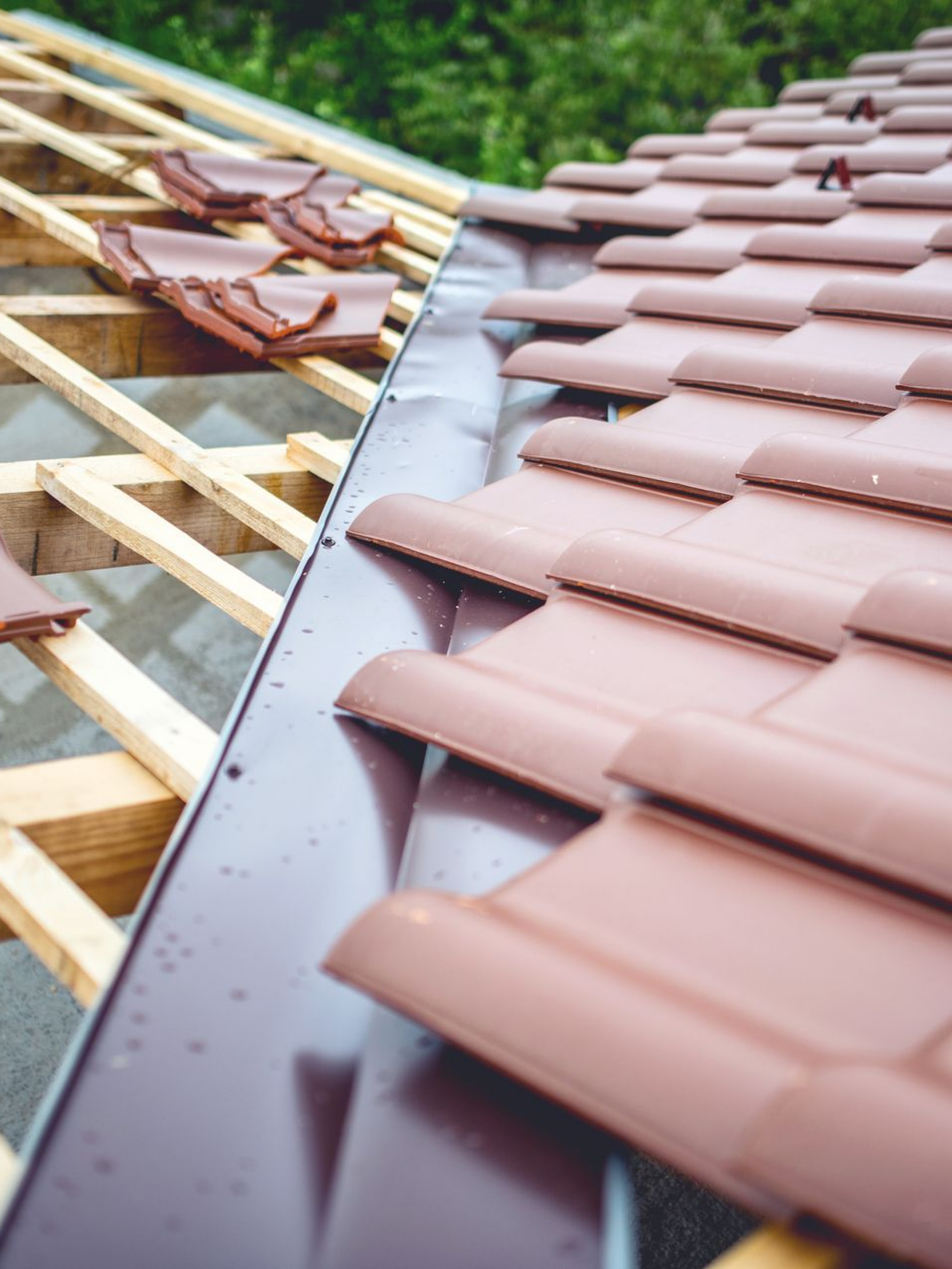 Pose de tuiles sur une toiture partiellement construite, avec des supports en bois apparents.