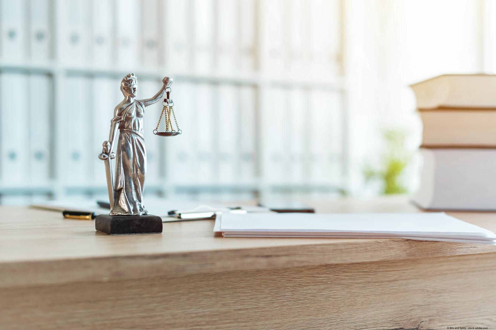 Justitia-Statue auf einem Schreibtisch mit Akten und Büchern.