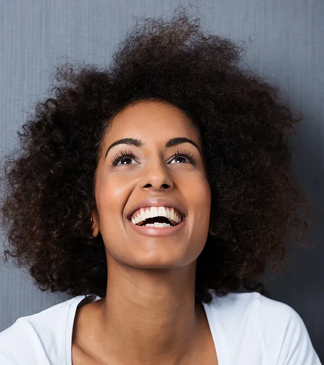 Una mujer con cabello rizado está sonriendo y mirando hacia arriba.