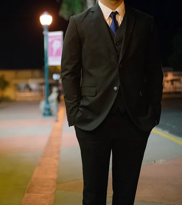 Un hombre con traje y corbata está de pie con las manos en los bolsillos.