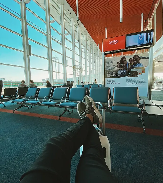 Una persona está sentada en la sala de espera de un aeropuerto con los pies sobre una maleta.