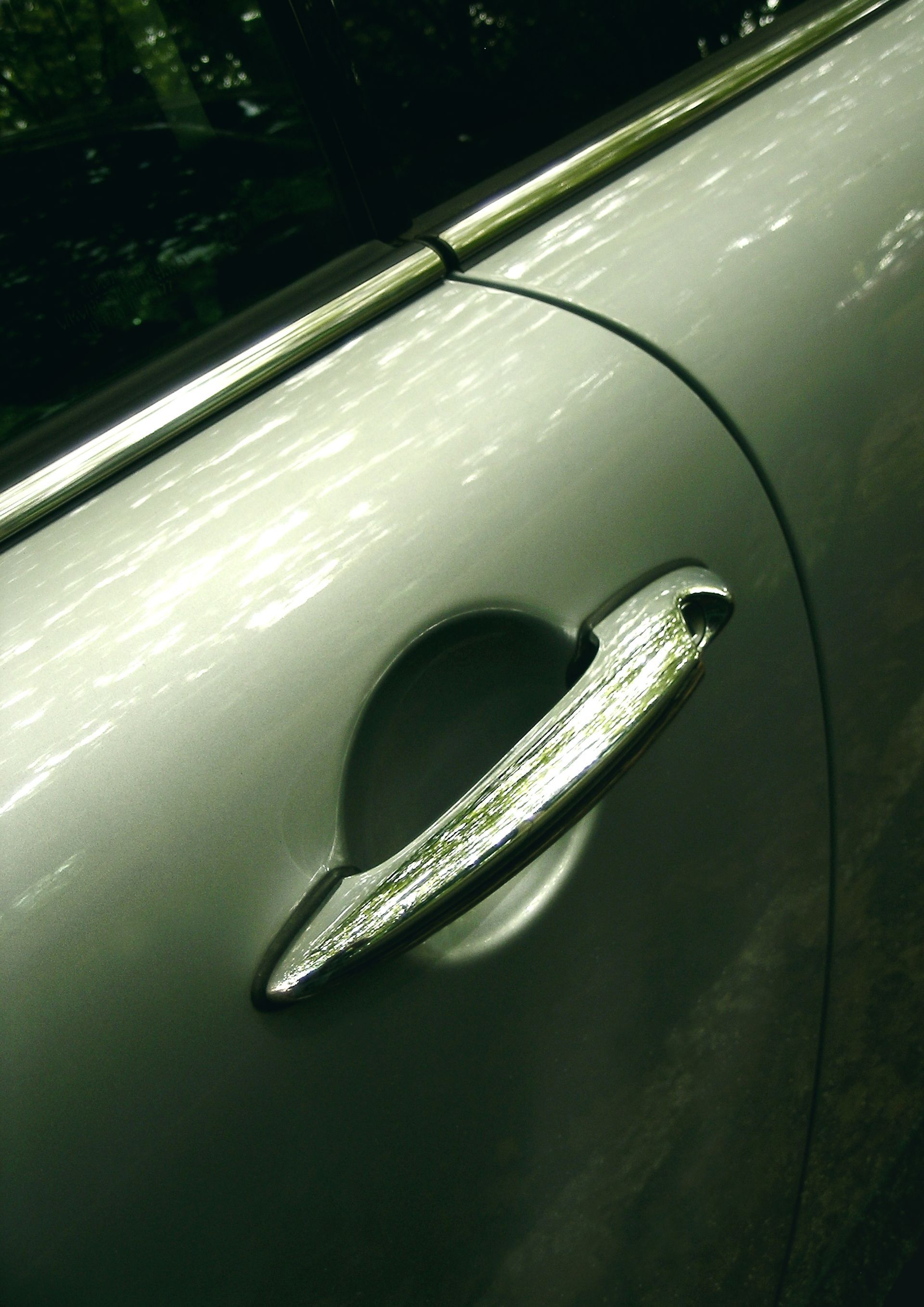 Gros plan sur une portière de voiture argentée présentant une poignée de porte horizontale, métallique et brillante.