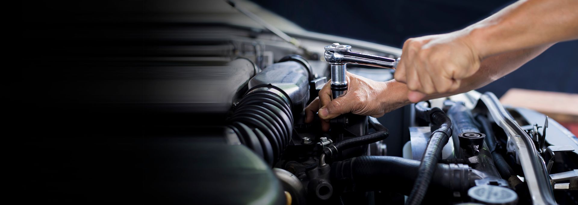 Les mains d'un mécanicien utilisant une clé à cliquet pour réparer un moteur de voiture.