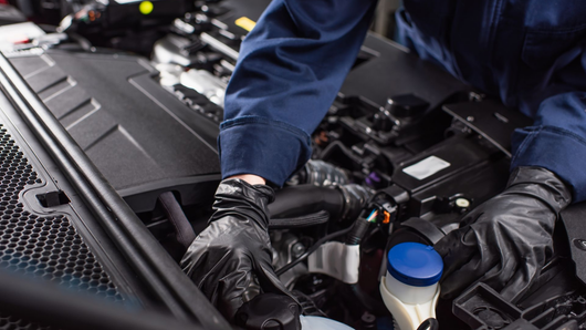 Un mécanicien portant une combinaison bleu foncé et des gants de protection noirs travaille sur un moteur de voiture.