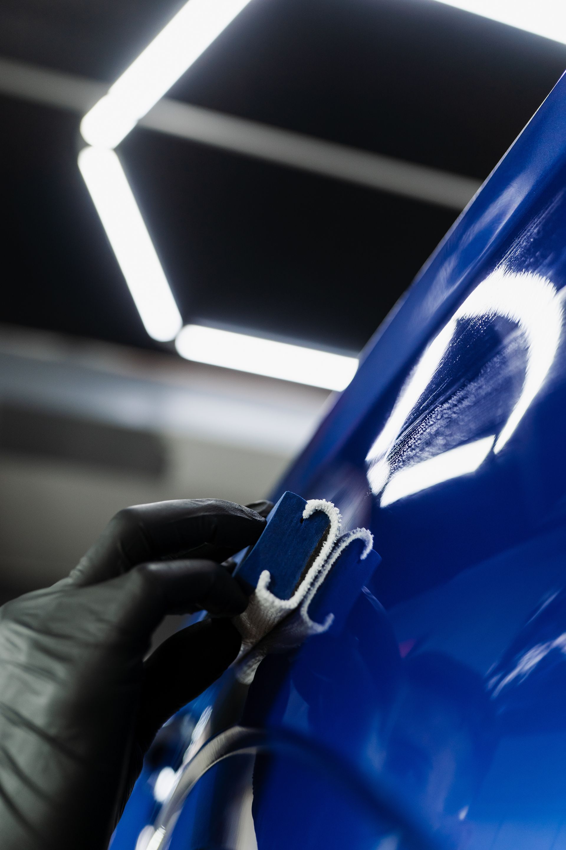 Sous la lumière vive de l'atelier, une main gantée utilise un applicateur blanc pour appliquer un revêtement.
