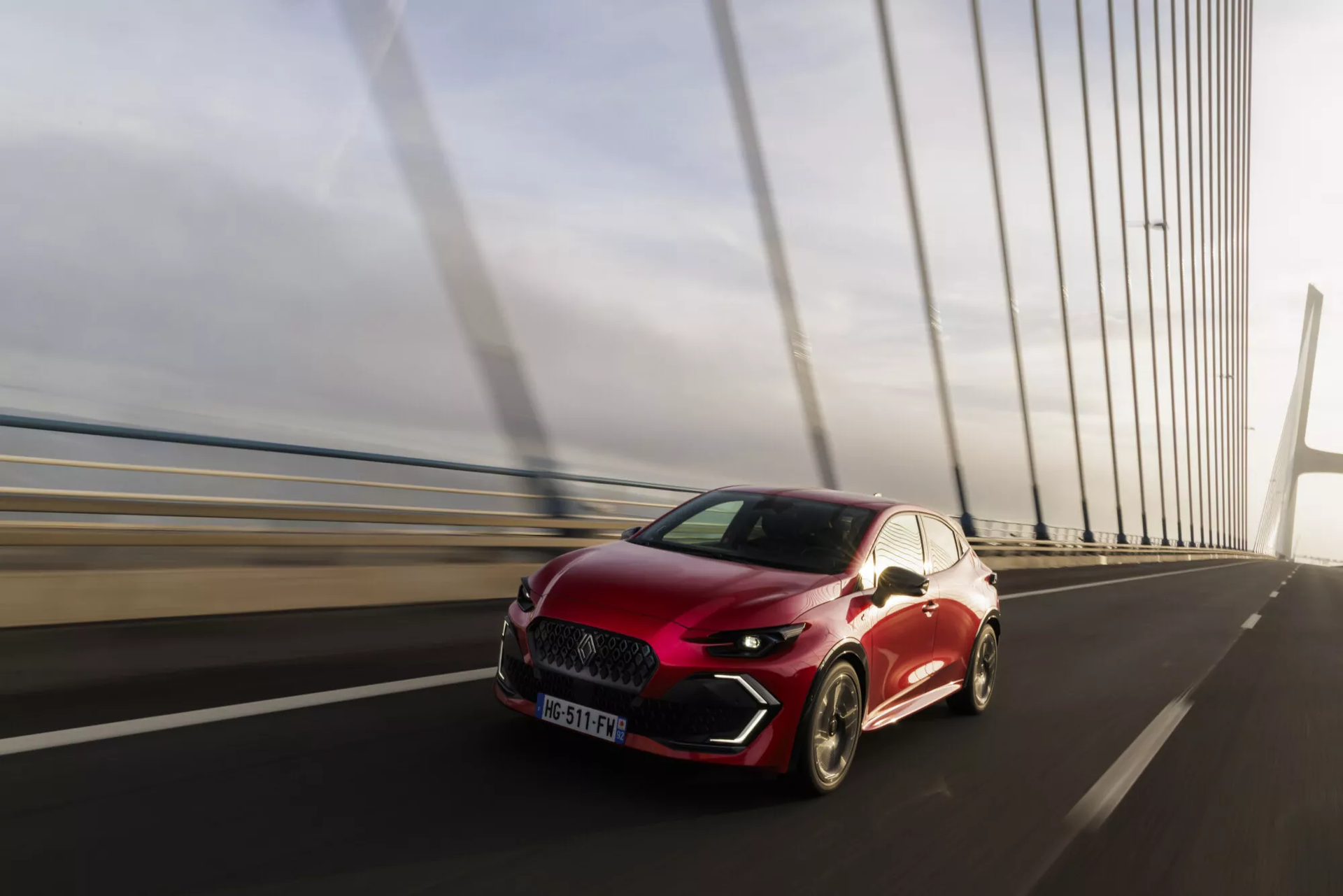 Une BMW DS4 rouge à hayon circulant en plein jour sur un pont à haubans moderne.