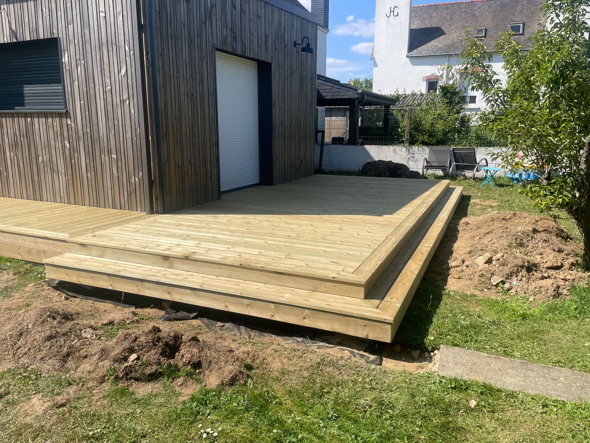 Terrasse en bois avec marches dans une cour, à côté d'un bâtiment aux panneaux de bois bruns.