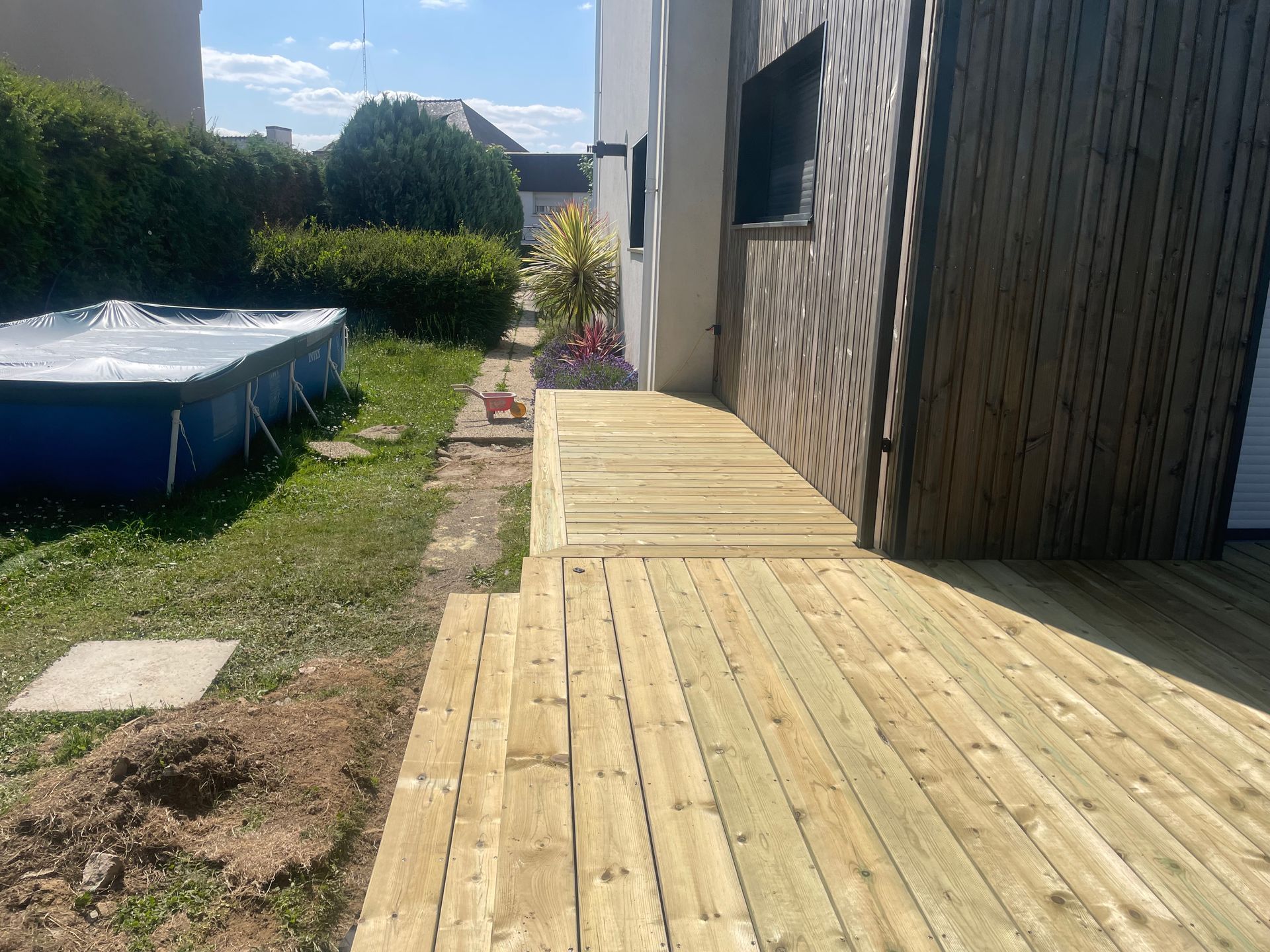 Terrasse en bois jouxtant une maison et un espace gazonné avec une petite piscine.