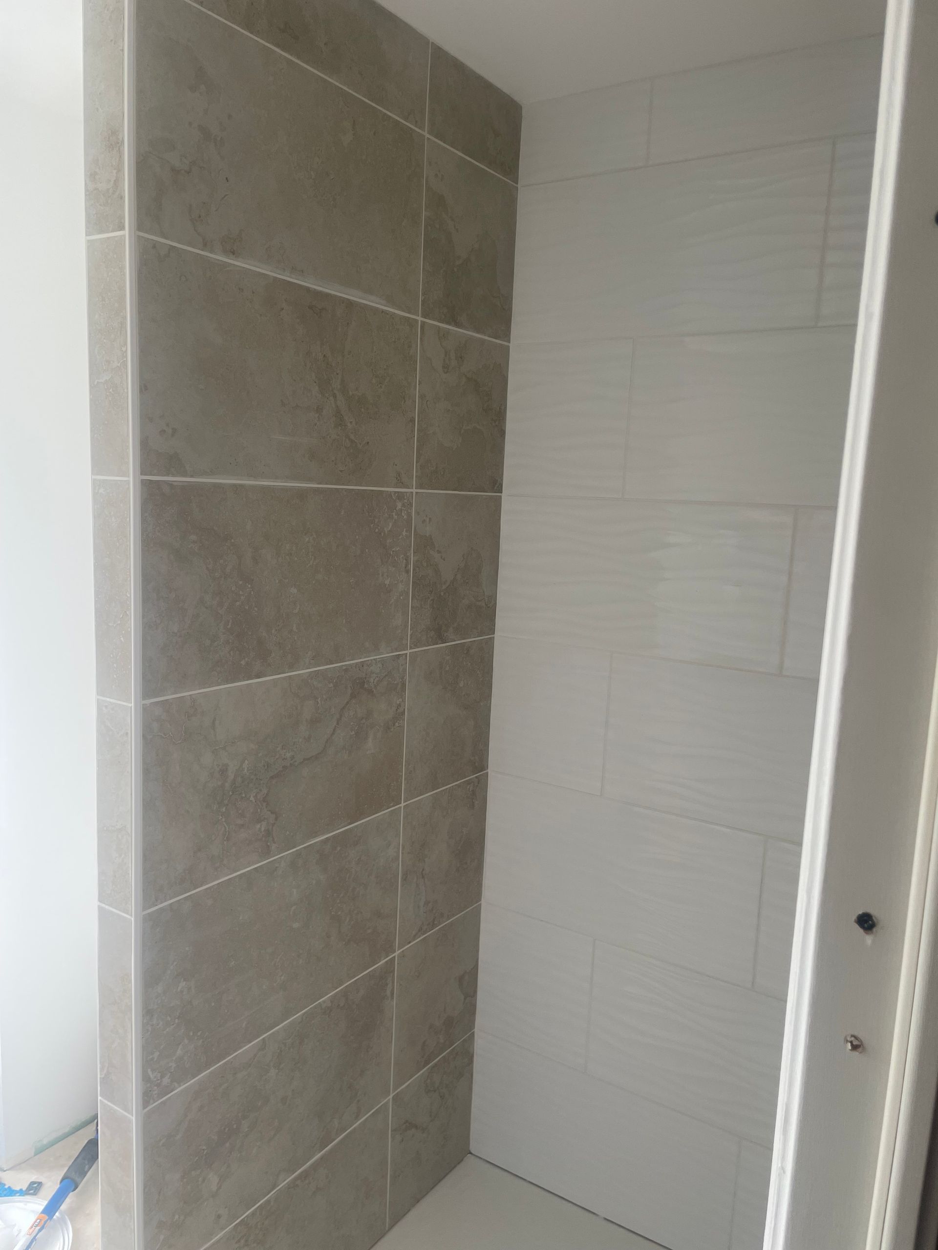 Douche en construction avec murs carrelés brun clair et blancs.