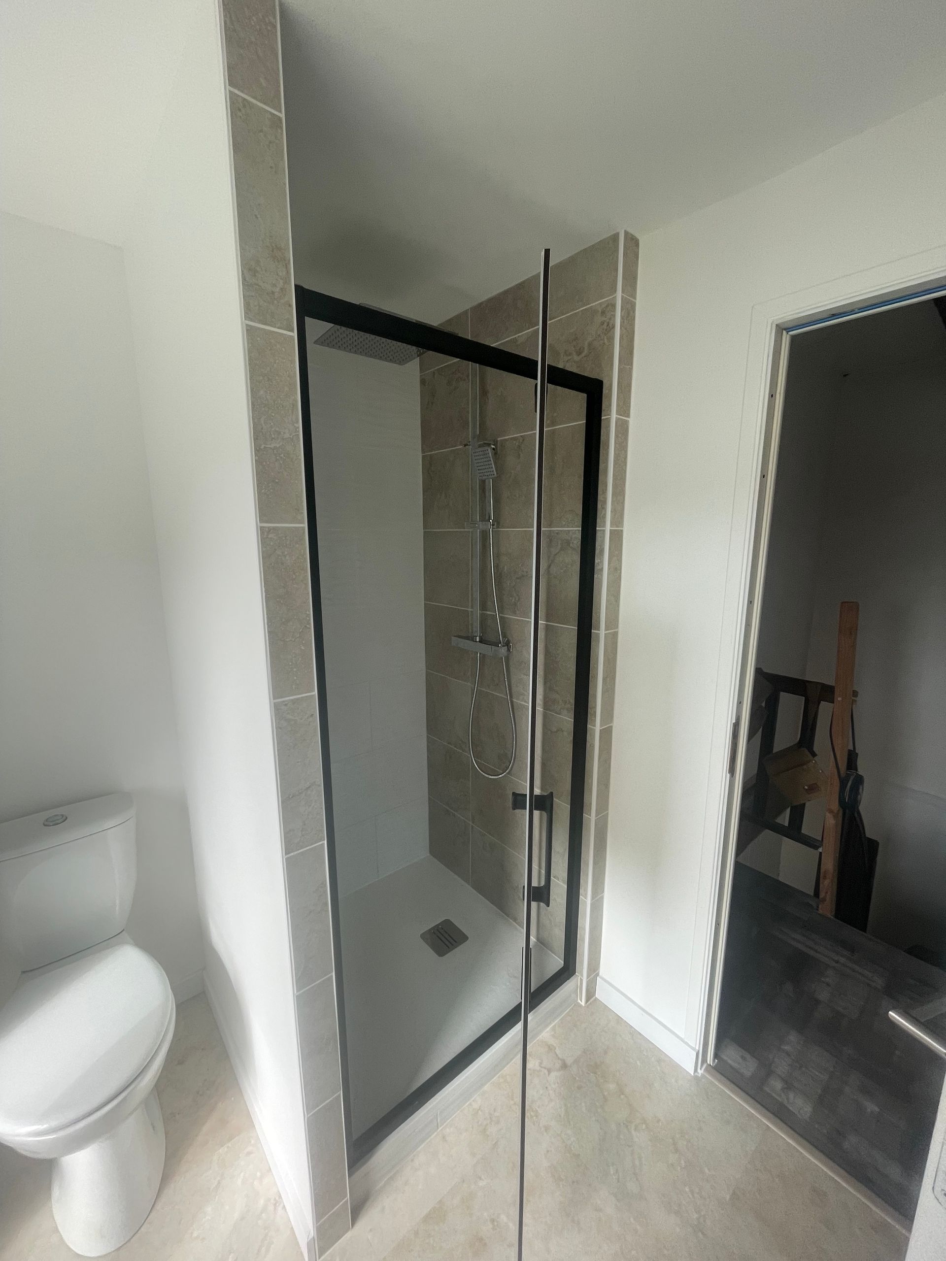 Cabine de douche avec cadre noir et porte en verre, murs carrelés et toilettes.