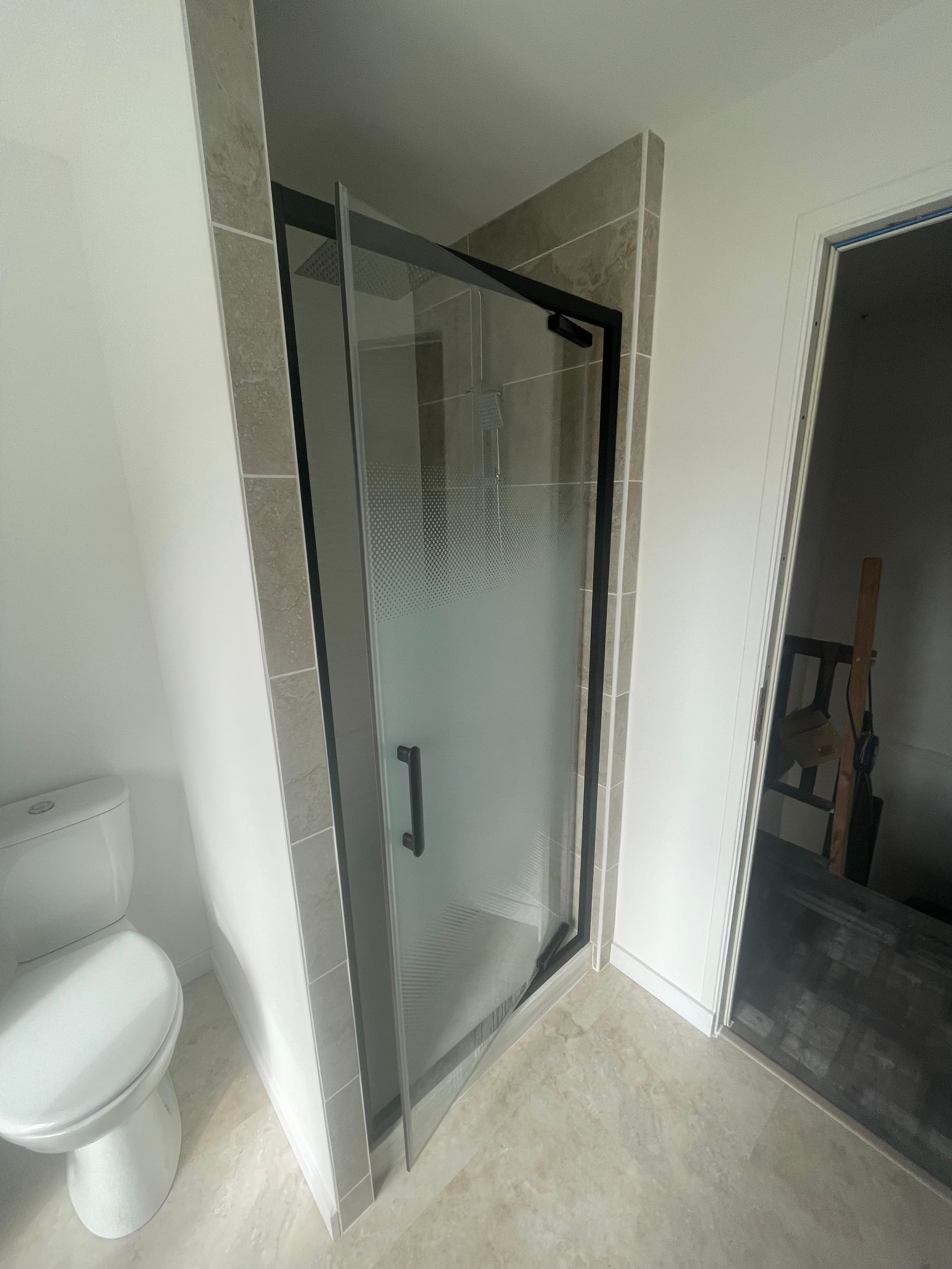 Cabine de douche avec garniture noire et porte en verre texturé, dans une salle de bains avec toilettes.