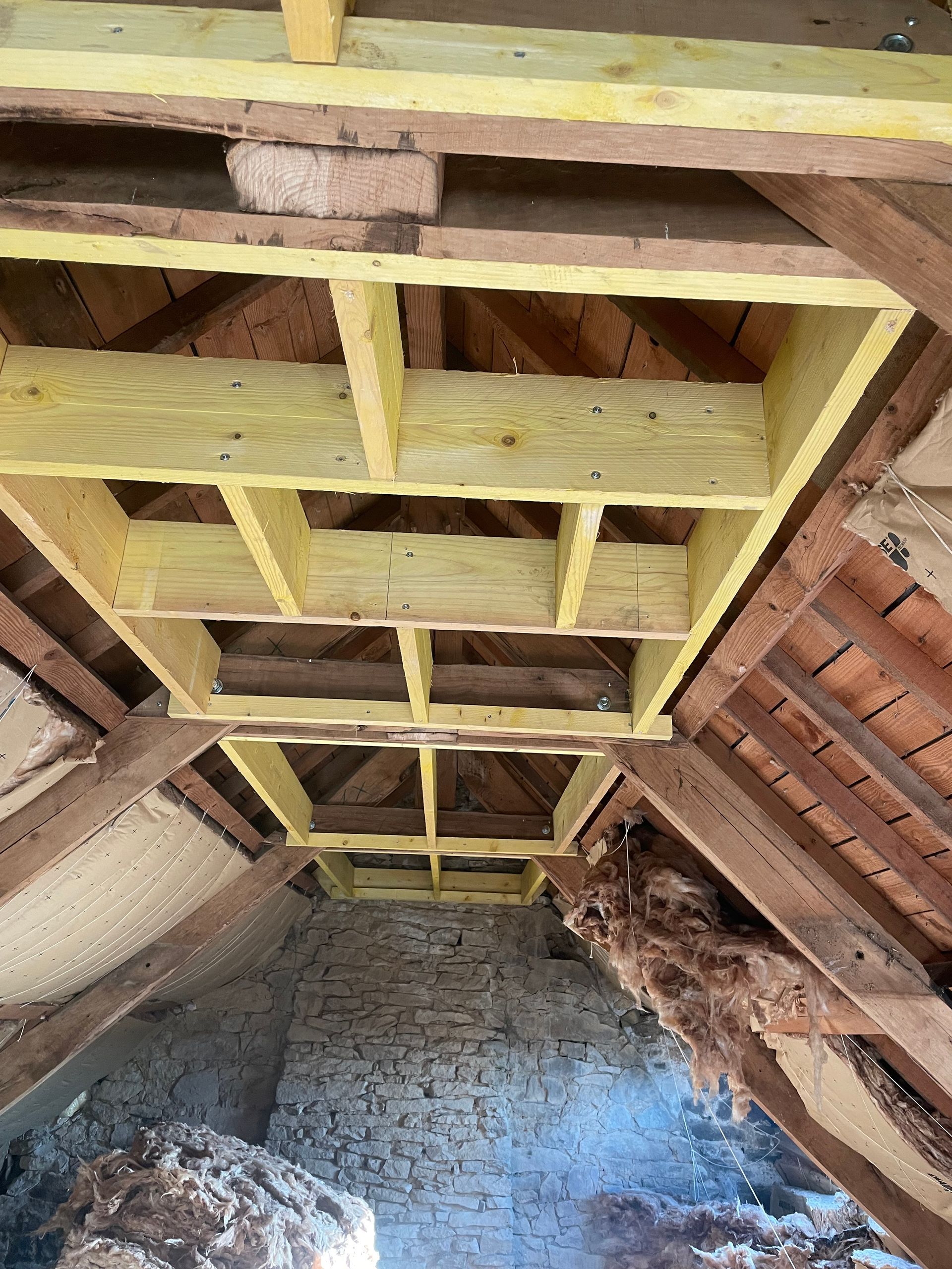 Plafond des combles en cours de construction, avec ossature en bois, isolation et maçonnerie apparentes.