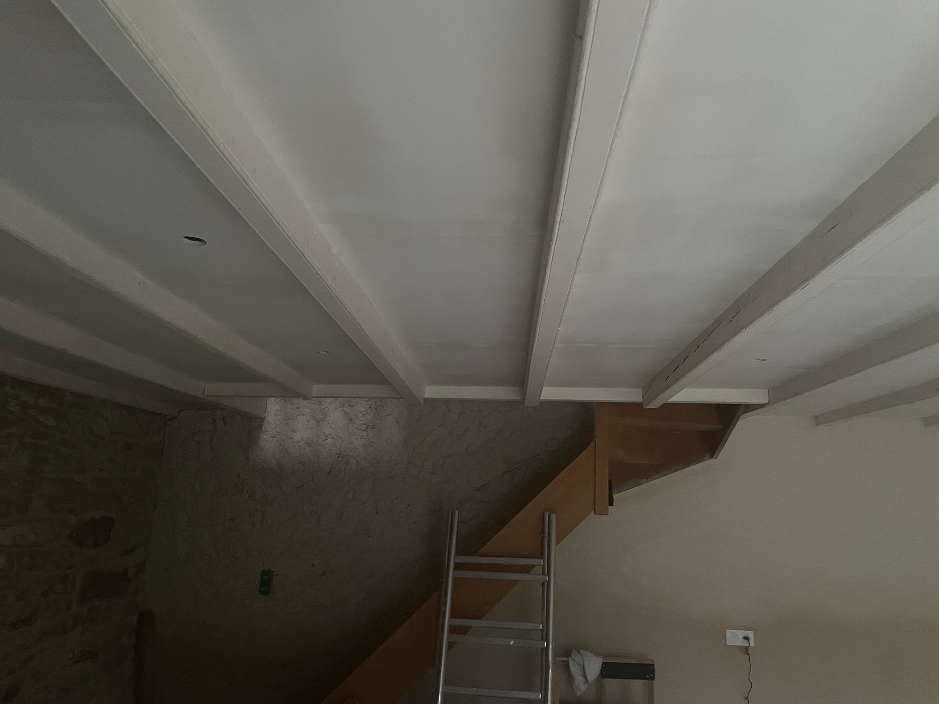 Poutres apparentes au plafond blanc, escalier et échelle à l'intérieur d'une pièce.