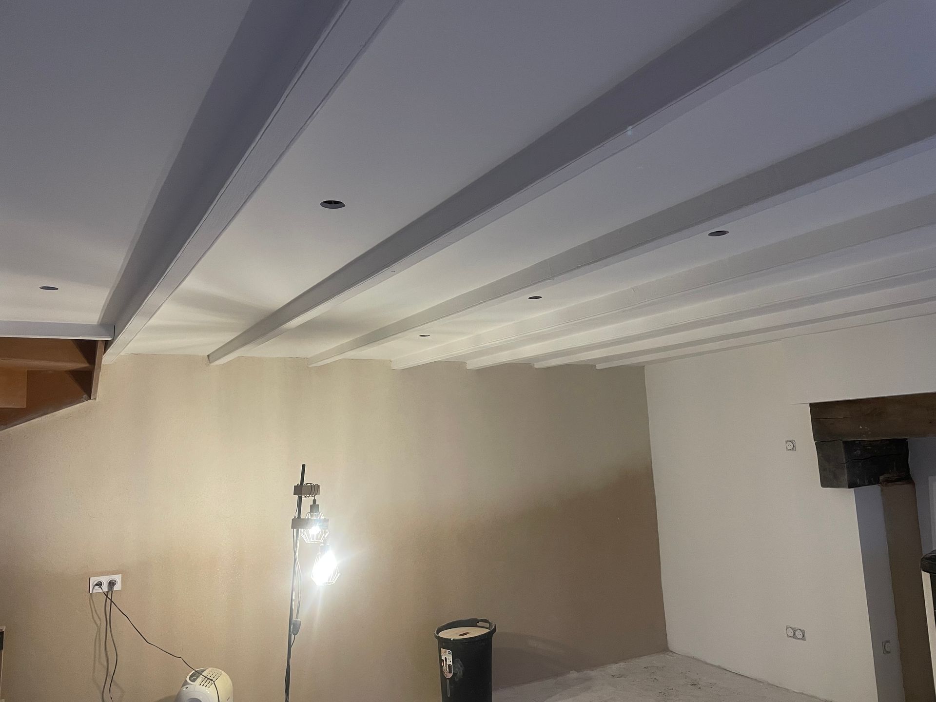 Pièce intérieure avec poutres blanches au plafond, éclairage encastré et murs beiges.