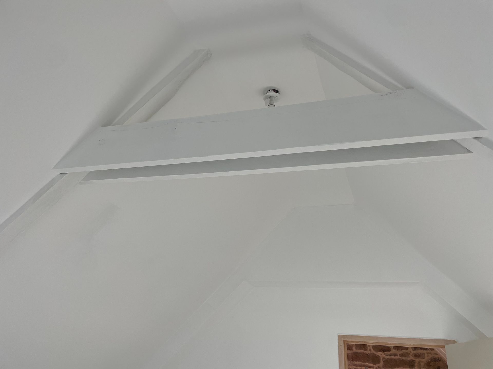 Plafond voûté blanc avec poutres triangulaires en bois et un luminaire.