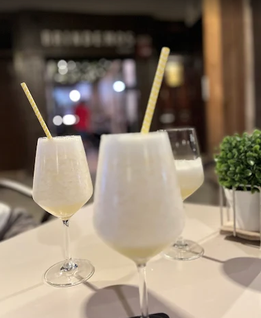 Tres cócteles espumosos con pajitas sobre una mesa, fondo interior borroso.