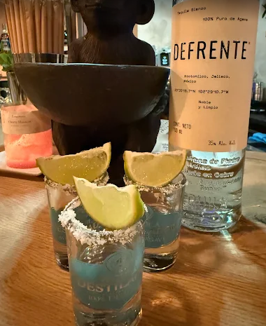 Tres shots de tequila con bordes de sal y gajos de limón, junto a una botella de tequila.