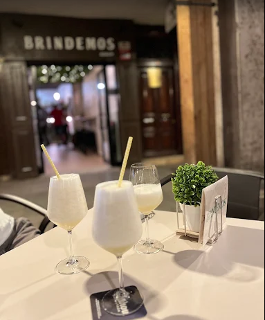 Tres bebidas blancas espumosas con pajitas en una mesa afuera de un bar con un cartel de 