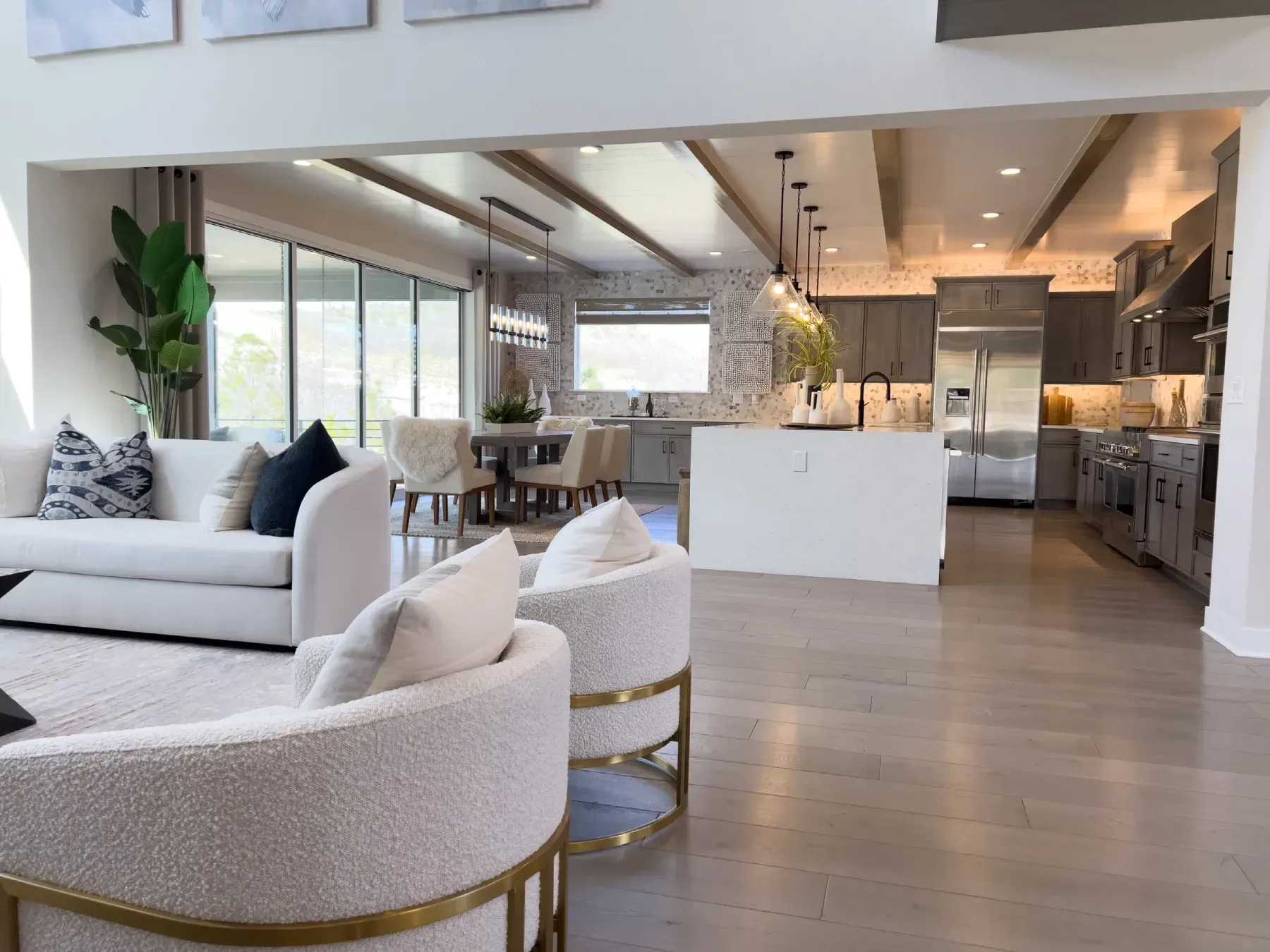 Salón-cocina moderno de planta abierta con muebles blancos, suelos de madera y grandes ventanales.