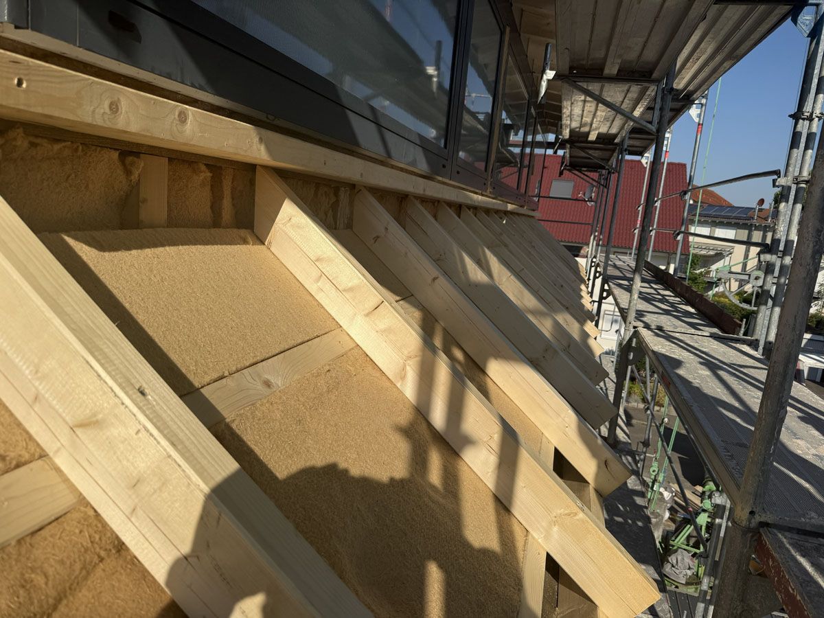 An einer Außenwand, die renoviert wird, werden Holzrahmen und Dämmplatten angebracht; in der Nähe befindet sich ein Gerüst.