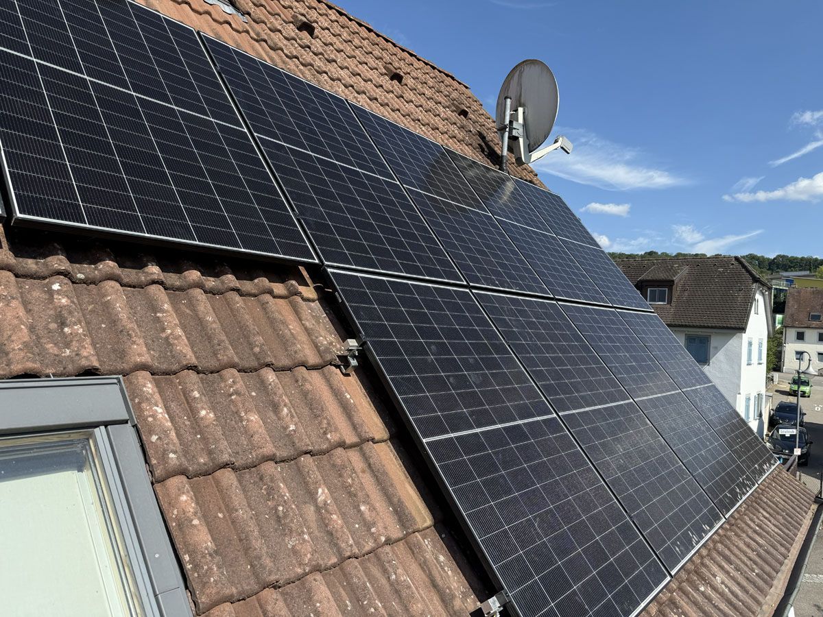 Schwarze Solarpaneele wurden auf einem mit braunen Terrakotta-Ziegeln gedeckten Wohnhausdach installiert, in der Nähe befindet sich eine Satellitenschüssel.