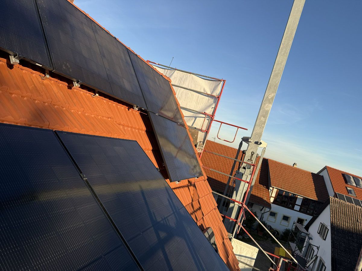 Auf einem schrägen, mit Terrakotta-Ziegeln gedeckten Dach sind Solarpaneele installiert, neben dem Gebäude ist unter blauem Himmel ein Gerüst zu sehen.