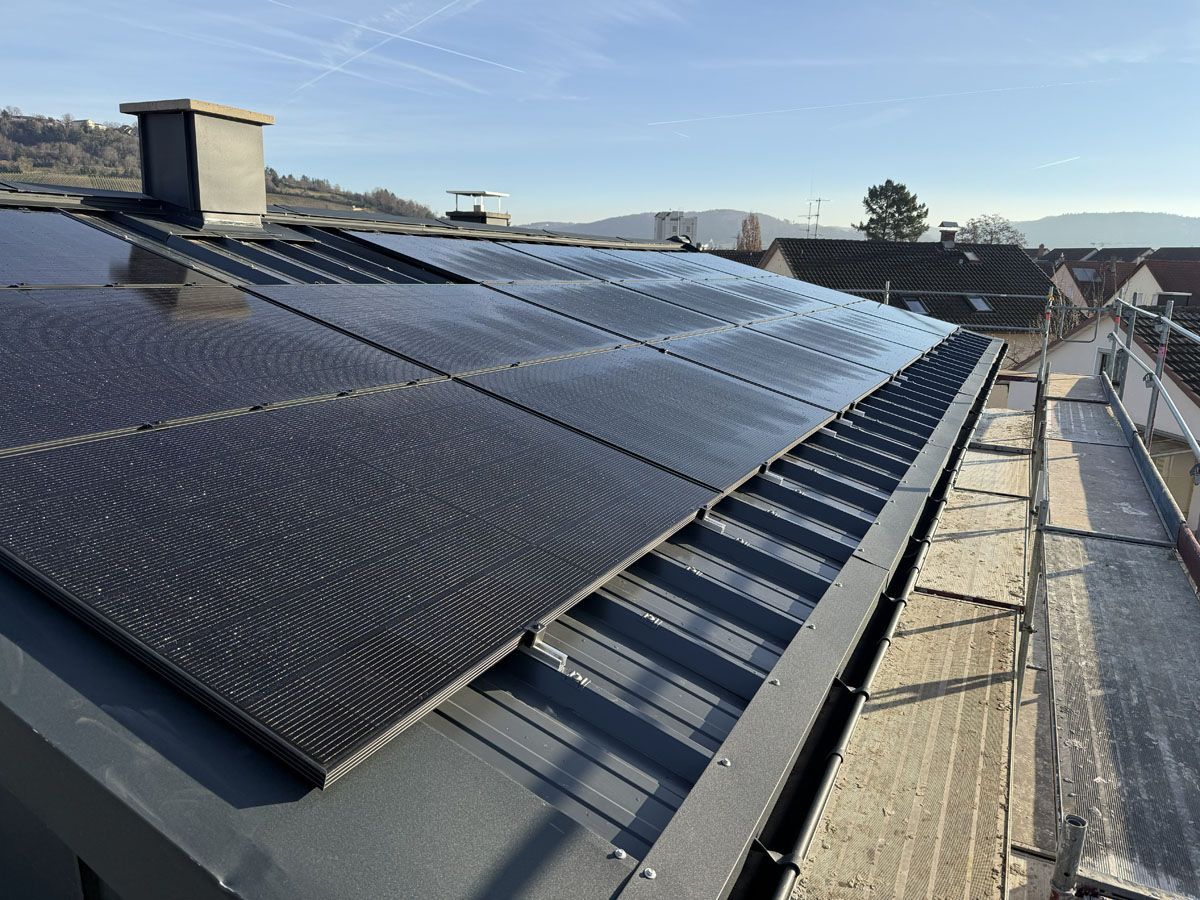 Eine Dachinstallation aus eleganten, schwarzen Solarmodulen auf einem Metalldach, an dessen Seite ein Gerüst sichtbar ist.